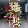 Kệ hoa hồng đỏ, cúc trắng và hướng dương nhỏ cùng dải ruy băng đỏ